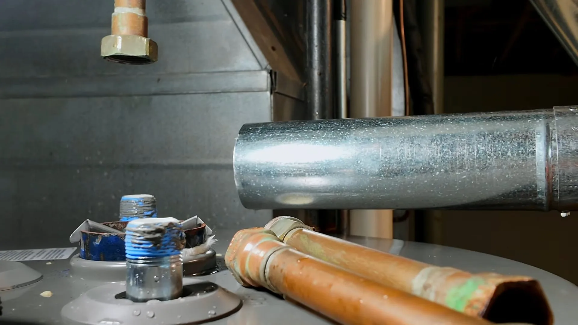 Copper supply pipes and a metal vent duct above the top of a tank water heater.