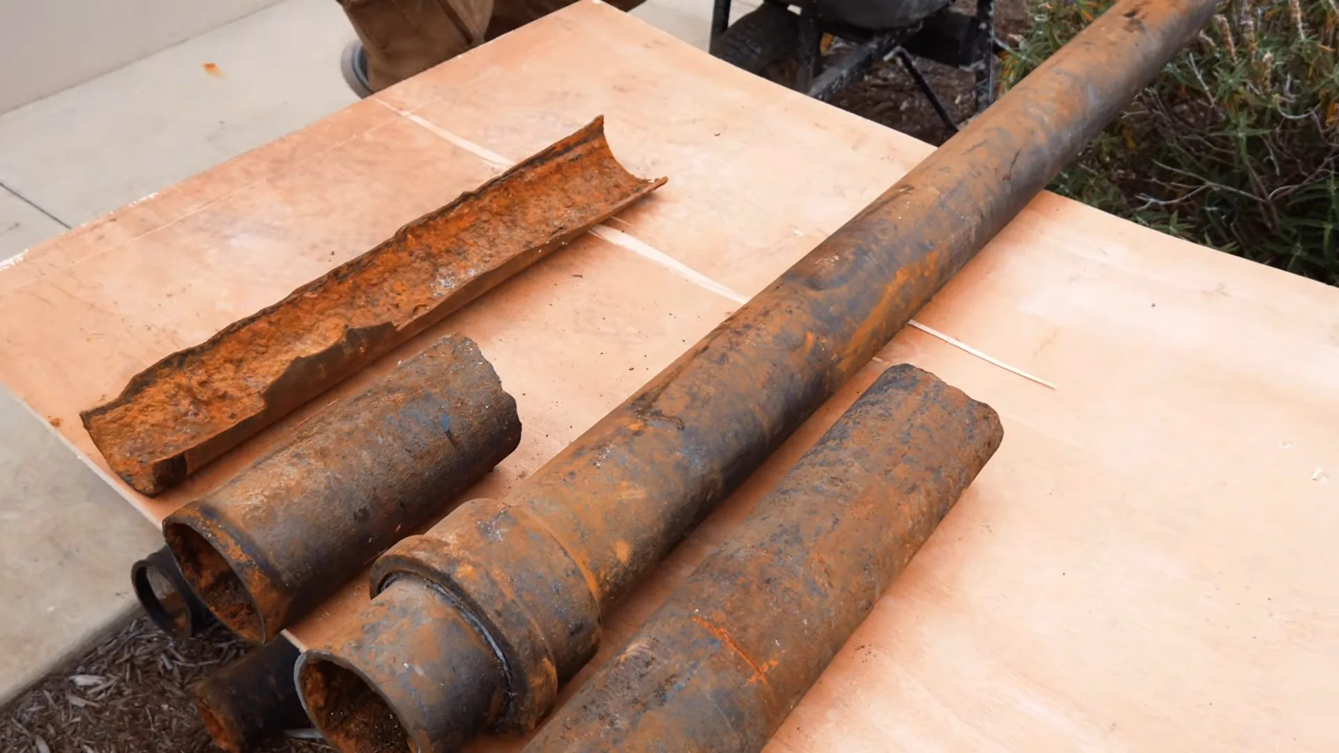 Four cut sections of rust-covered steel pipe lying on a wooden board, one split open lengthwise.