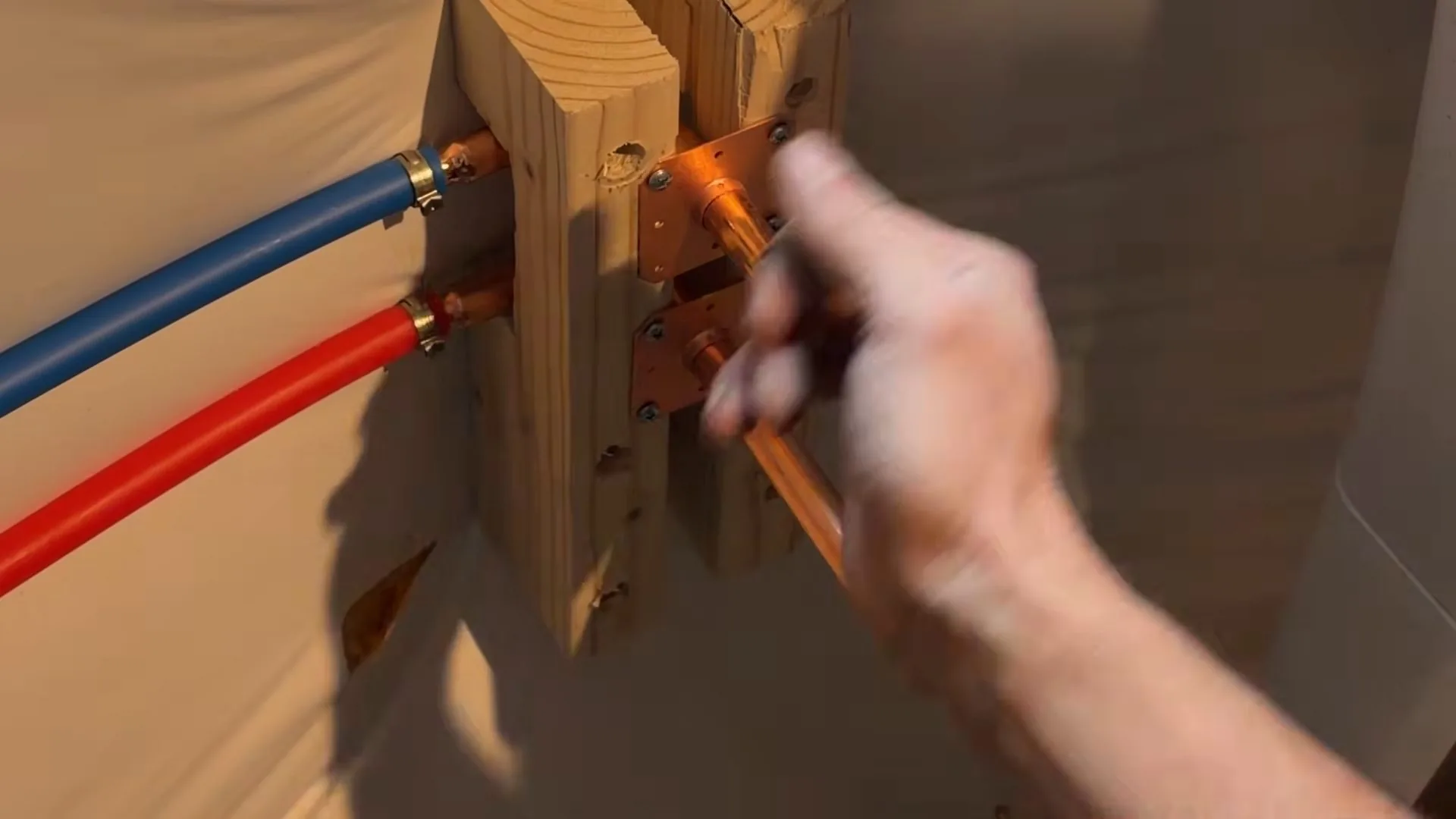 A hand adjusting a copper connection on a wooden block with red and blue PEX tubing attached.