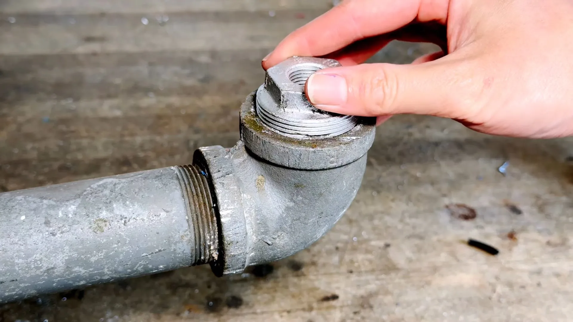 Hand unscrewing the threaded cleanout plug on a galvanized drain trap.