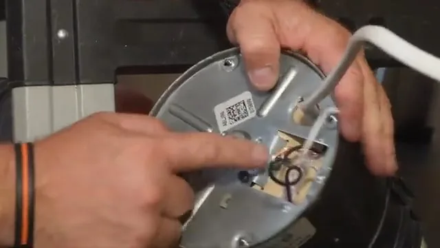 Hands pointing to the wiring compartment on the underside of a garbage disposal.