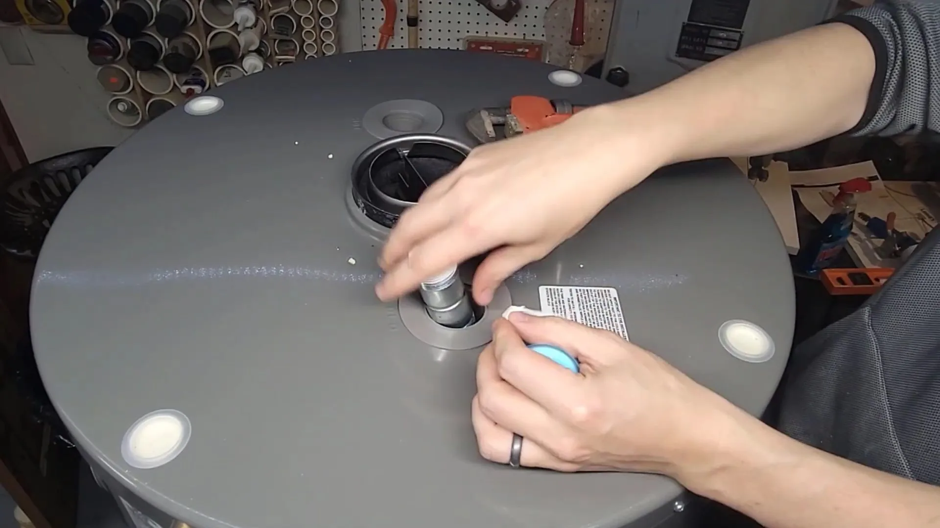 Hands working on a fitting on top of a gray water heater tank.