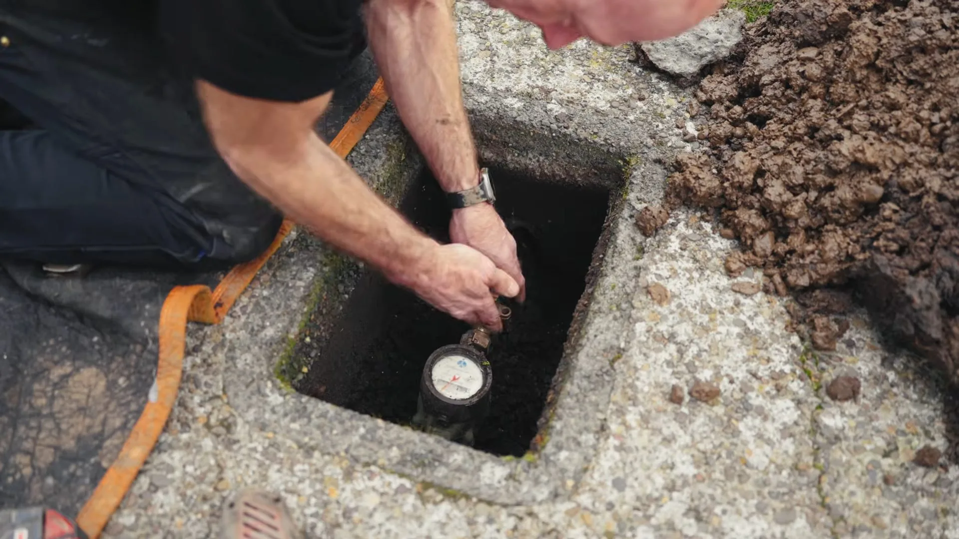 Man kneeling beside an open water meter box and reaching down to the meter.