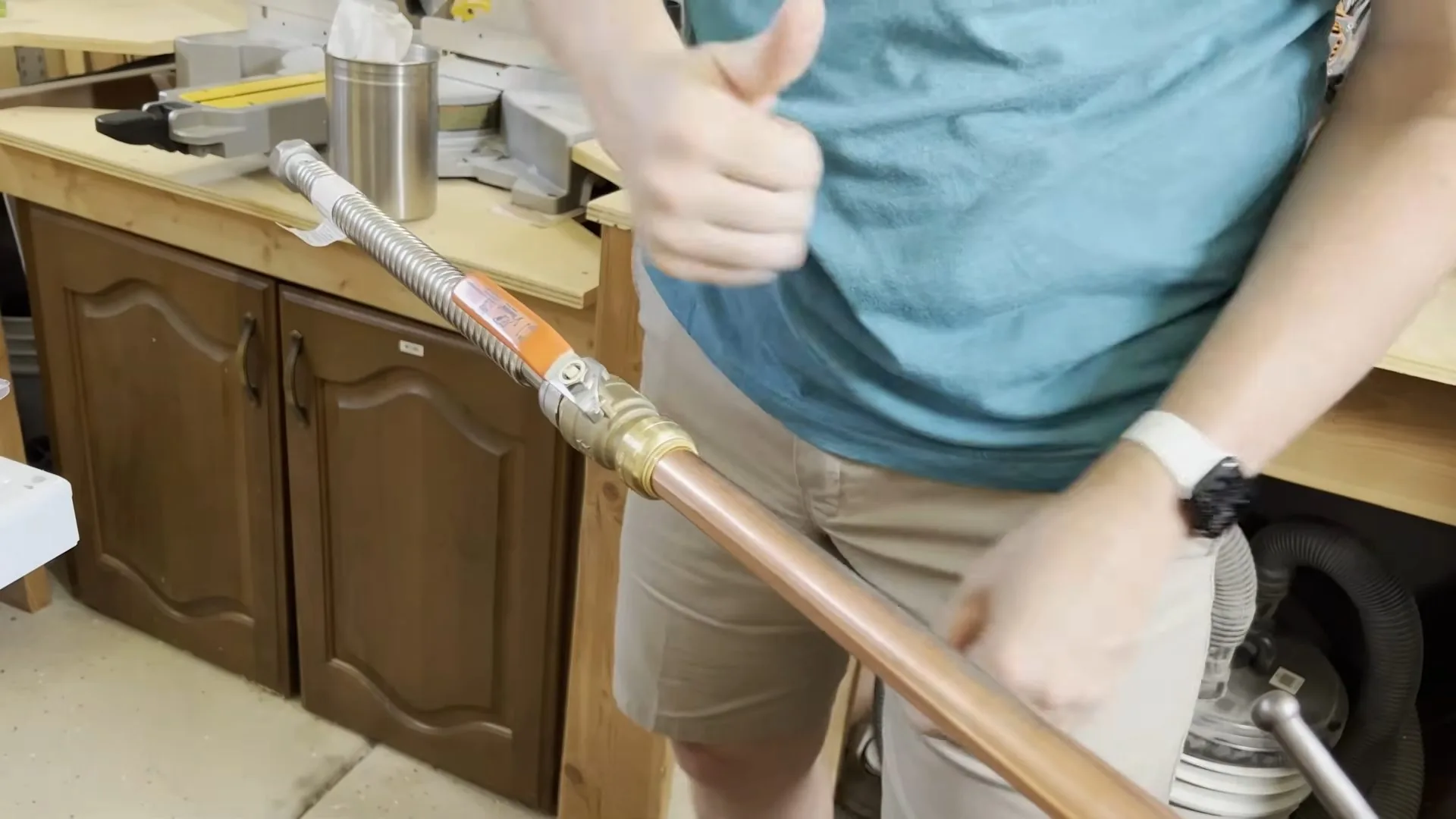 Person giving a thumbs up beside a length of copper pipe fitted to a brass connector.