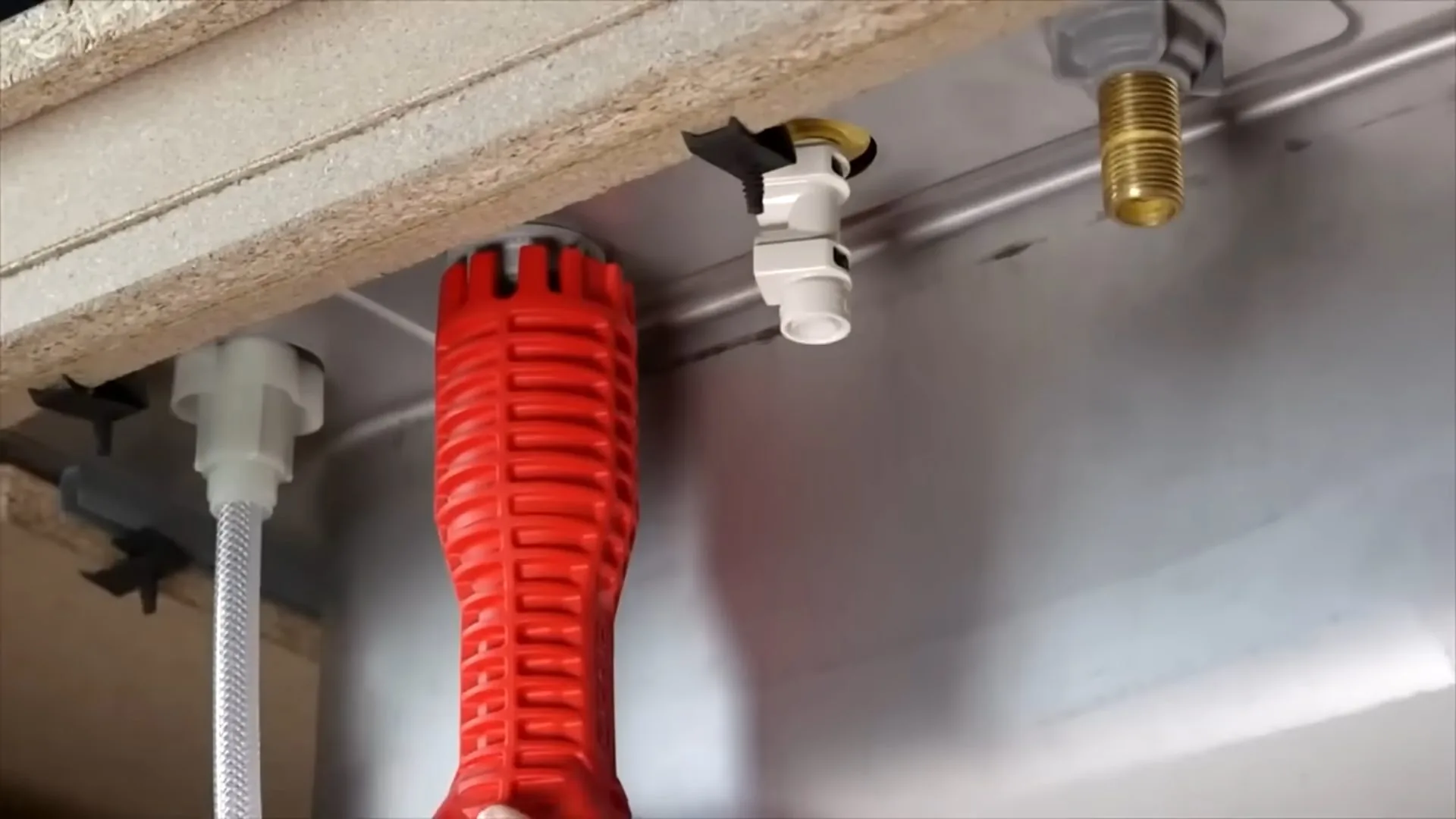 Red faucet tool resting under a sink beside shutoff valves and supply lines.