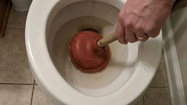 Hand pressing a red plunger into a toilet bowl.