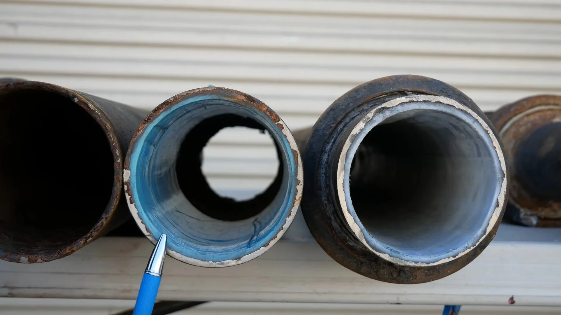 Three steel pipe ends side by side, the middle one lined in blue and white, with a blue pen pointing at the liner.