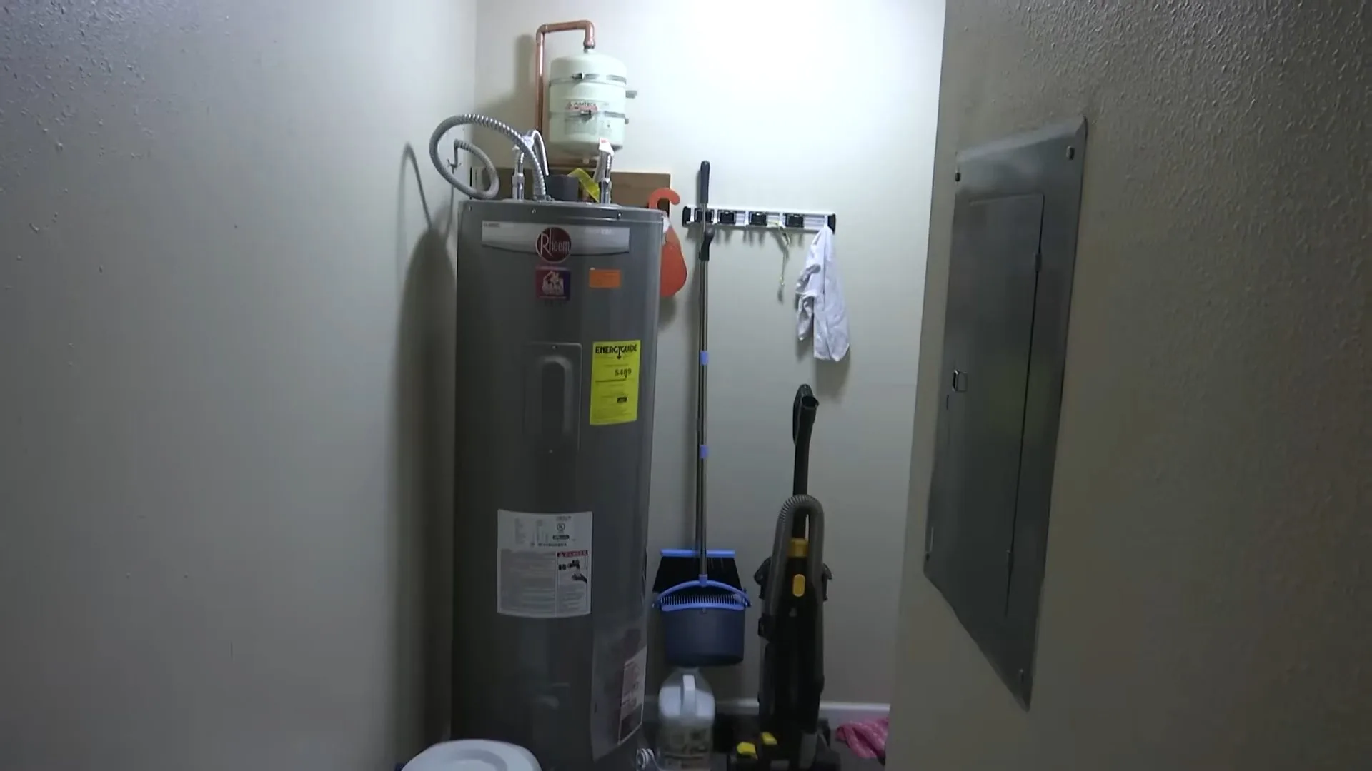 Tank water heater standing in a utility room beside an electrical panel.