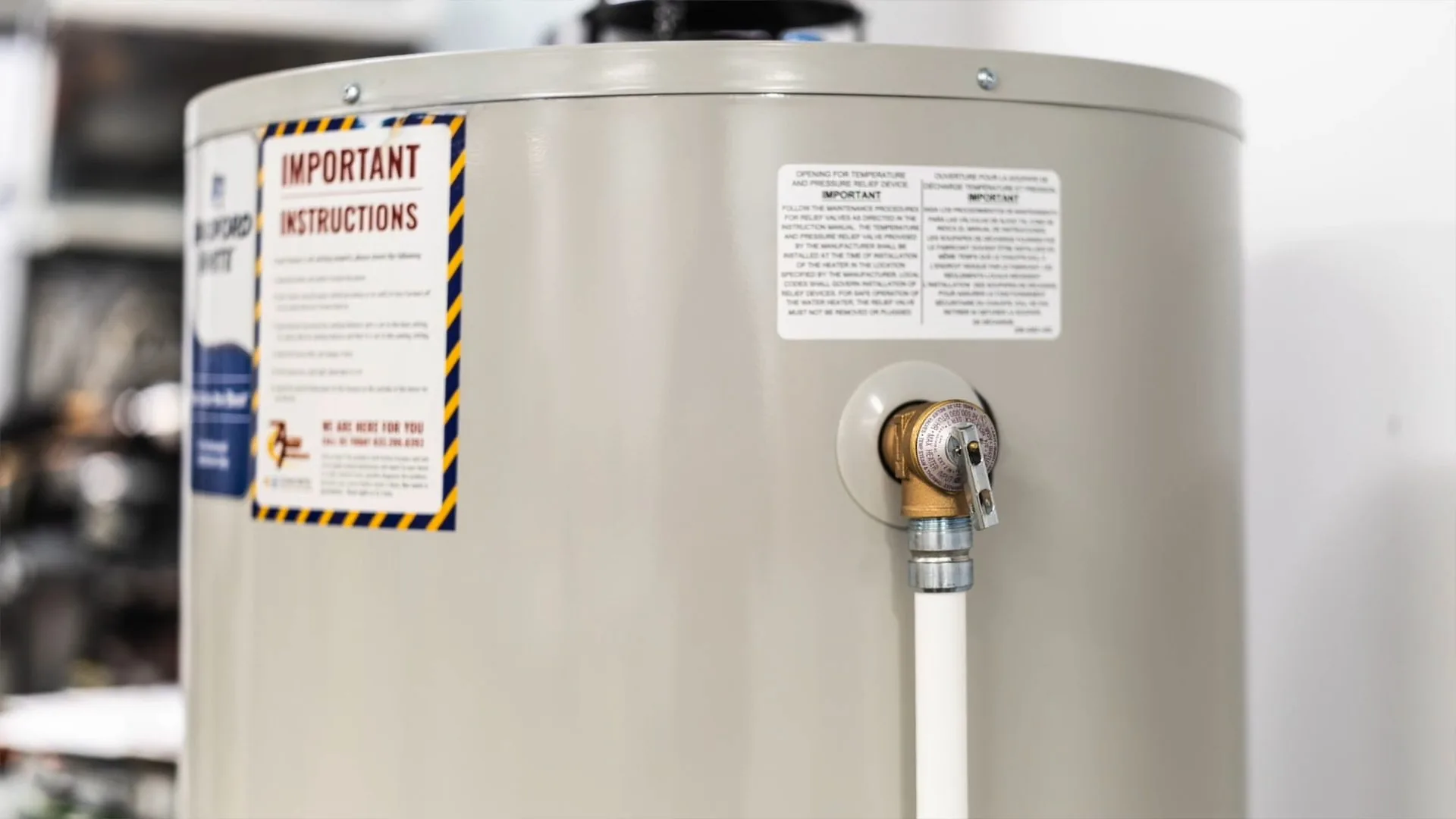 Tank water heater showing its warning label and a supply fitting with a white tube attached.