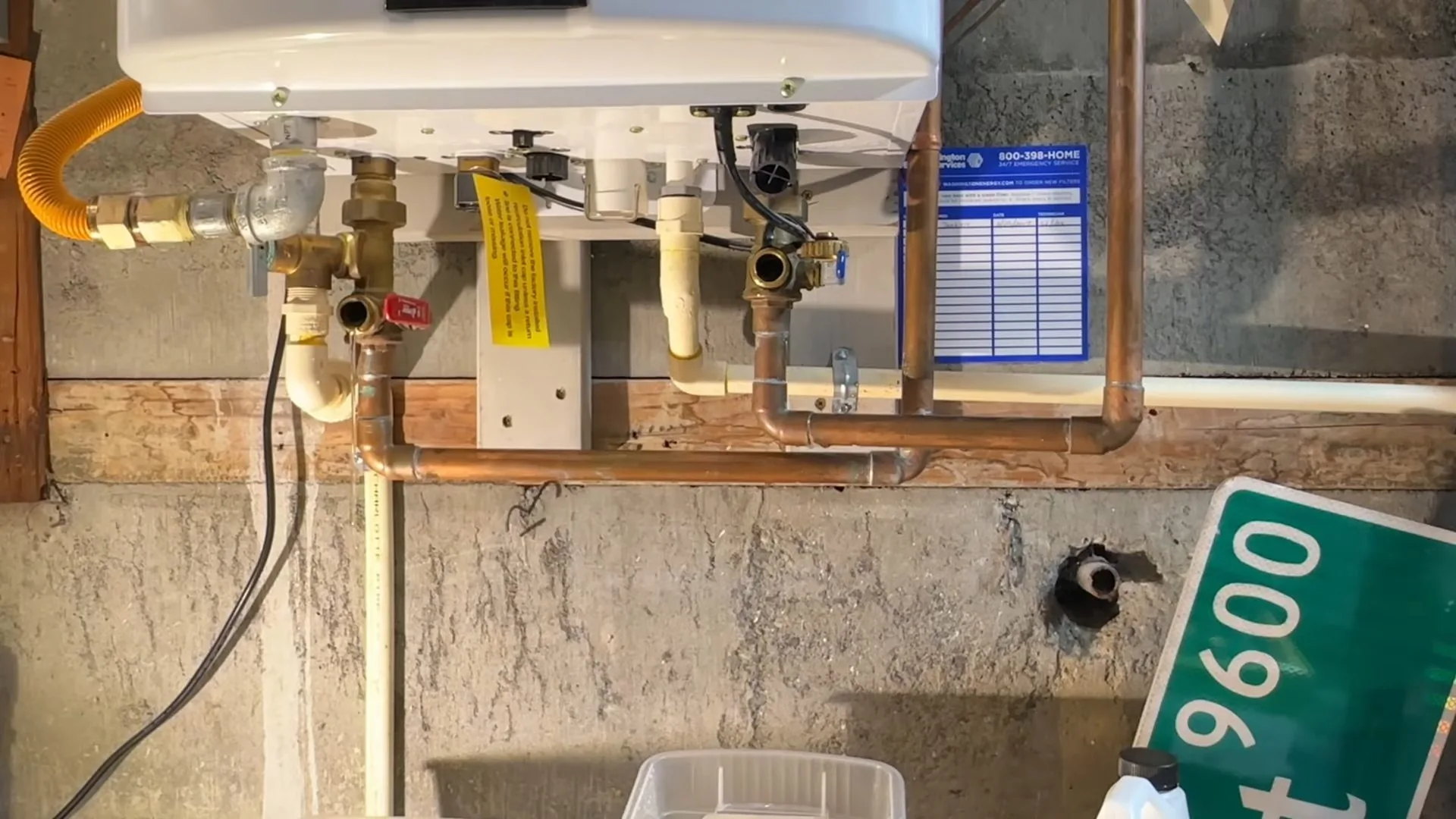 Tankless water heater mounted high on a wall with a yellow gas line, copper pipes and valves below it.