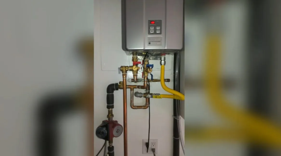 Wall-mounted tankless water heater with copper water lines, a yellow gas line and a small circulation pump below it.