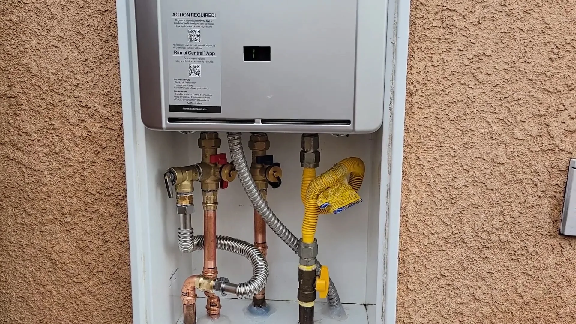Wall-mounted tankless water heater in an exterior wall cabinet, with gas and water lines below it.